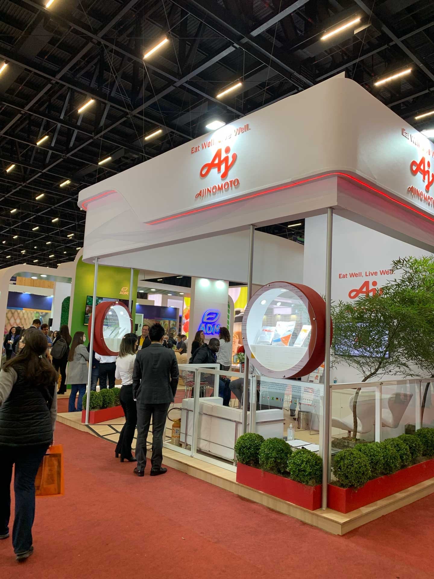Outro ângulo do estande da Ajinomoto, com as vitrines circulares vermelhas em primeiro plano e o lounge de reuniões ocupado ao fundo.