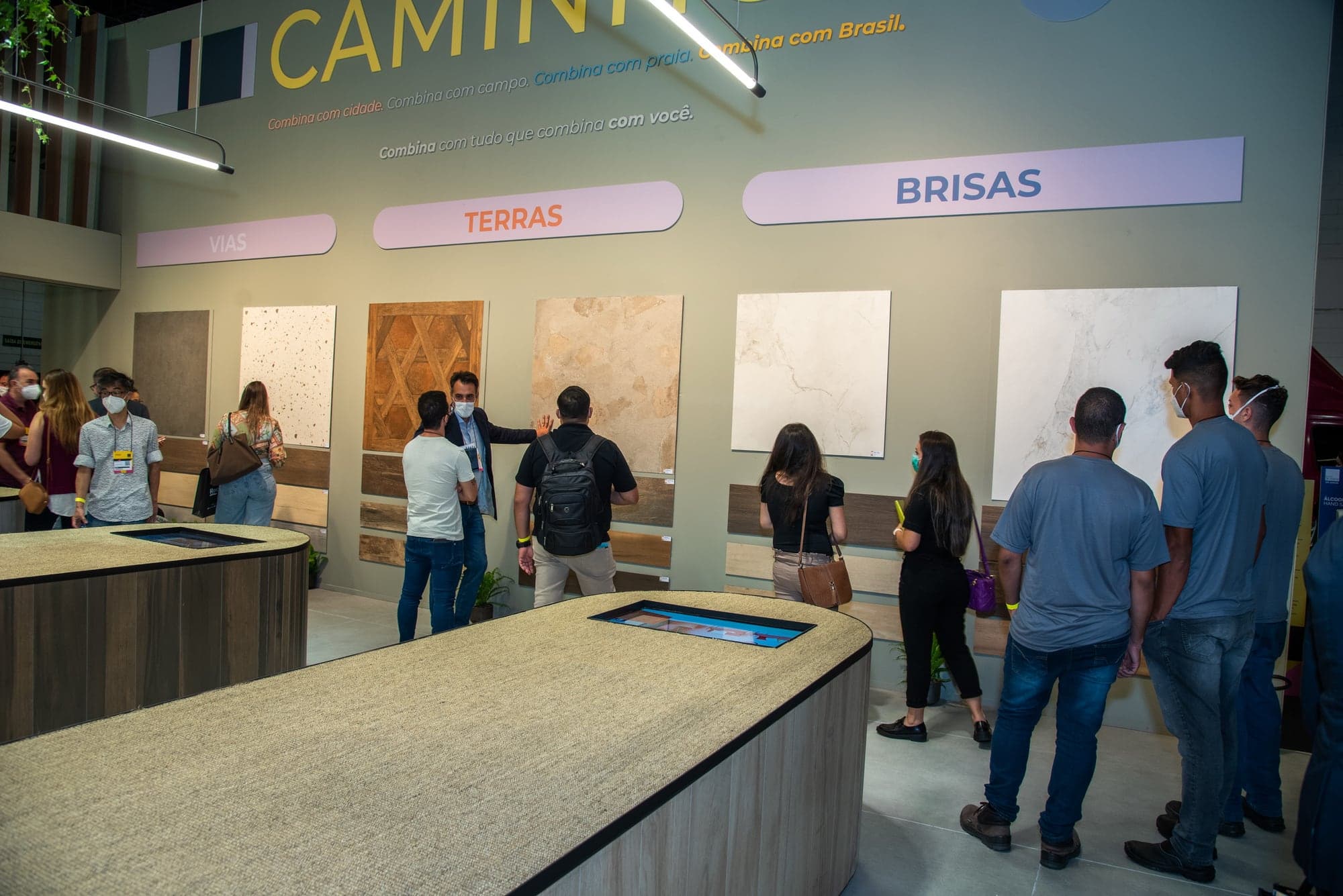 Parede principal do estande da Elizabeth com o título Caminhos e a frase 'Combina com cidade. Combina com campo. Combina com praia. Combina com Brasil', abaixo da qual três placas nomeiam as zonas Vias, Terras e Brisas, com amostras de revestimento montadas na parede.
