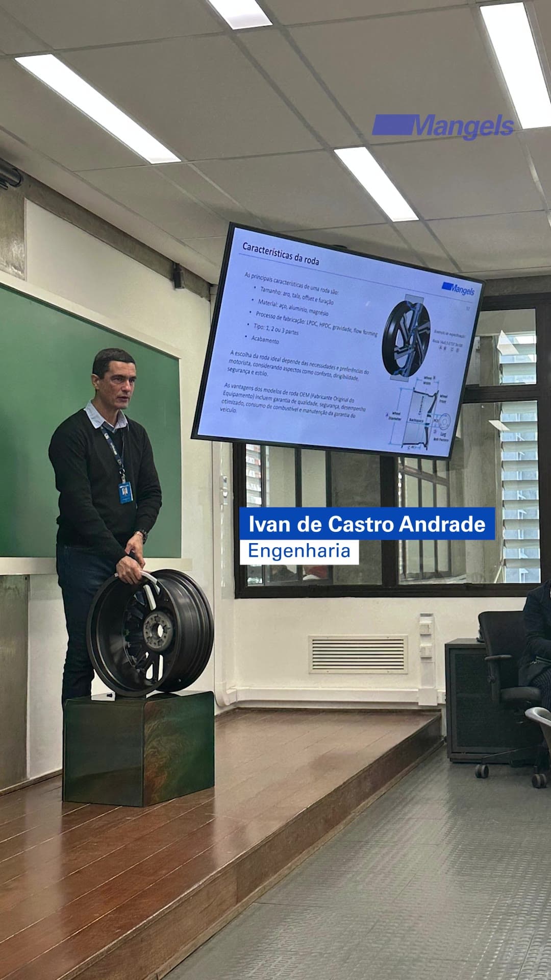 Sala de aula no Instituto Mauá: um engenheiro da Mangels apresenta as características técnicas da roda diante de uma tela com o desenho técnico, ao lado de uma roda de alumínio sobre um pedestal.