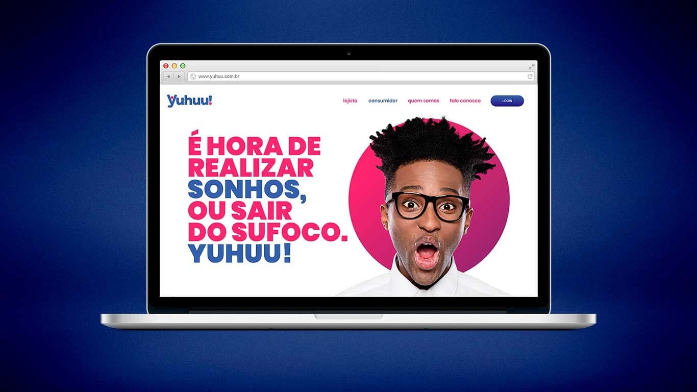 Home do site da Yuhuu num notebook: menu com as entradas lojista e consumidor, e a chamada 'É hora de realizar sonhos, ou sair do sufoco. Yuhuu!' ao lado da foto de um homem com expressão de surpresa alegre.